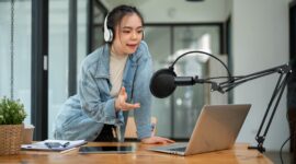 A beautiful and professional Asian female radio host or radio journalist is speaking into a microphone, announcing special news during her on-air radio show in her studio.