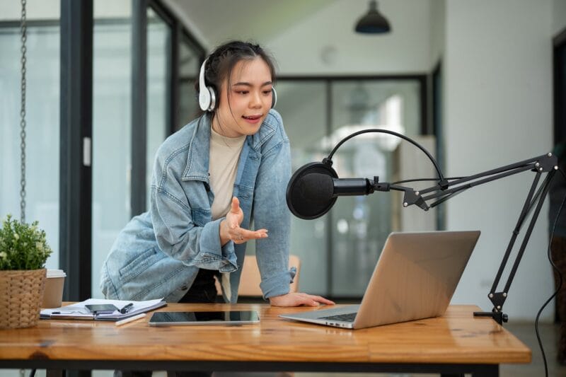 A beautiful and professional Asian female radio host or radio journalist is speaking into a microphone, announcing special news during her on-air radio show in her studio.