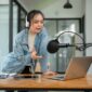 A beautiful and professional Asian female radio host or radio journalist is speaking into a microphone, announcing special news during her on-air radio show in her studio.