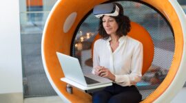 Businesswoman with taken off VR headset giving product review. Woman in office clothes and virtual reality goggles sitting in interactive chair and using laptop. VR product test concept