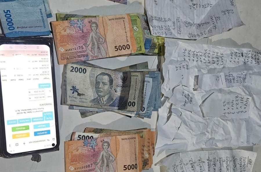 Barang bukti uang tunai Rp4,1 juta, lembaran kertas rekapan angka, kartu ATM, dan satu unit telepon genggam yang disita dari tersangka judi togel online M di Karupuak Tabiang, Padang, Senin (26/10/2026) malam.